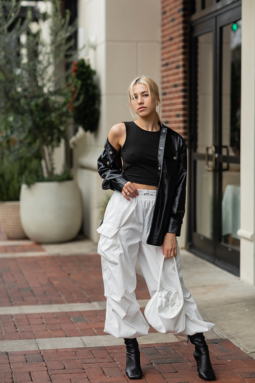 full length of young blonde woman in leather shirt jacket posing with handbag on street in Miami