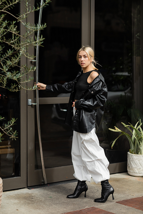 full length of stylish woman in leather shirt jacket and cargo pants opening entrance door on street in Miami