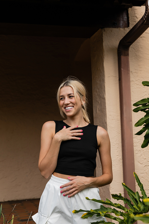 cheerful young woman in trendy clothes standing near modern house in Miami