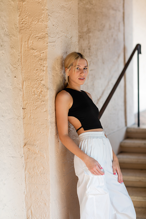 blonde woman in stylish outfit standing near wall of modern house in Miami