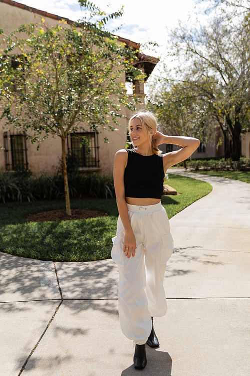 full length of cheerful woman in trendy clothes standing near modern house in Miami