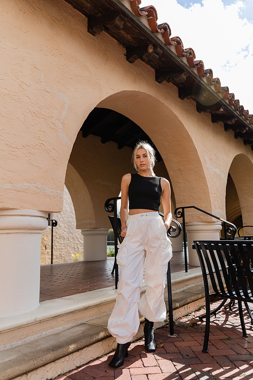 full length of blonde woman in stylish outfit standing near modern house in Florida