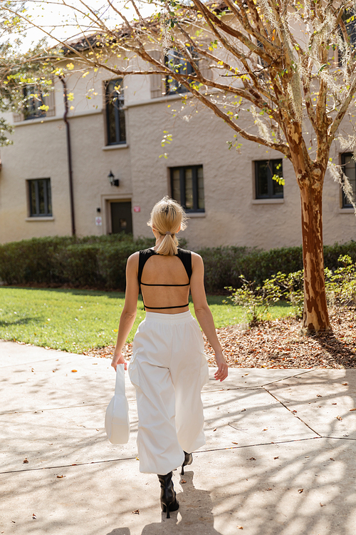 back view of blonde woman with handbag walking near house in Miami