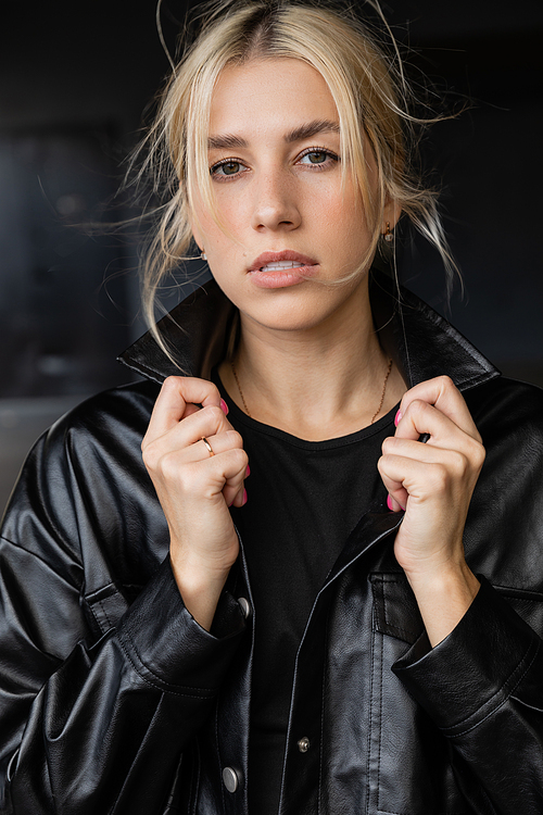 portrait of young blonde woman adjusting collar of leather shirt jacket