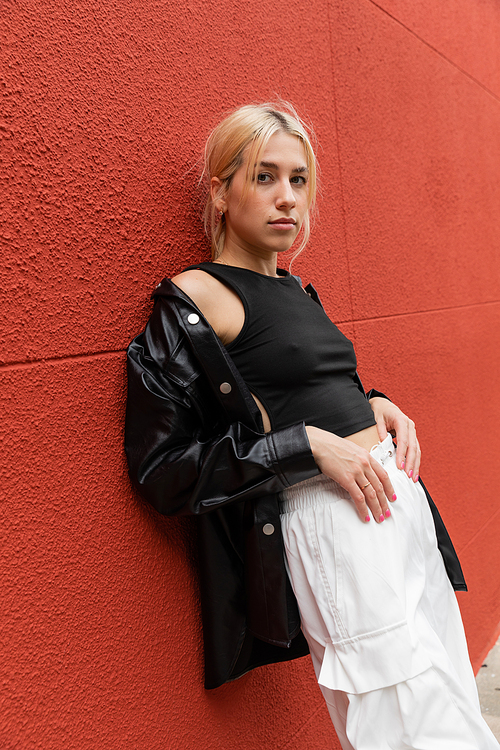 blonde woman in cargo pants and leather shirt jacket standing near red wall in Miami