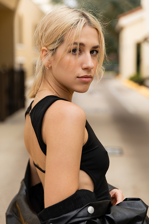 portrait of blonde young woman in black tank top looking at camera outdoors