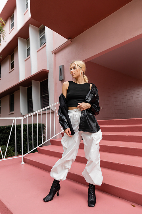 full length of blonde young woman in black tank top and cargo pants standing on pink stairs in Miami