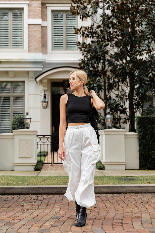 full length of blonde woman walking with leather shirt jacket near house in Miami