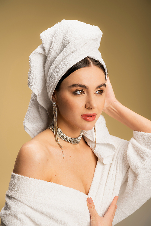 pretty woman in luxurious jewelry posing with towel on head on beige