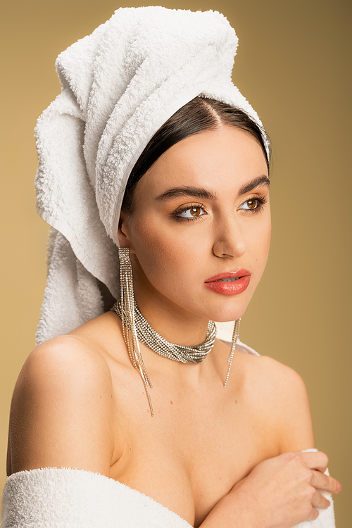 young woman in luxurious jewelry posing with towel on head on beige