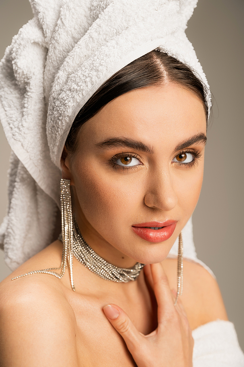 young woman in luxurious jewelry posing with towel on head isolated on grey