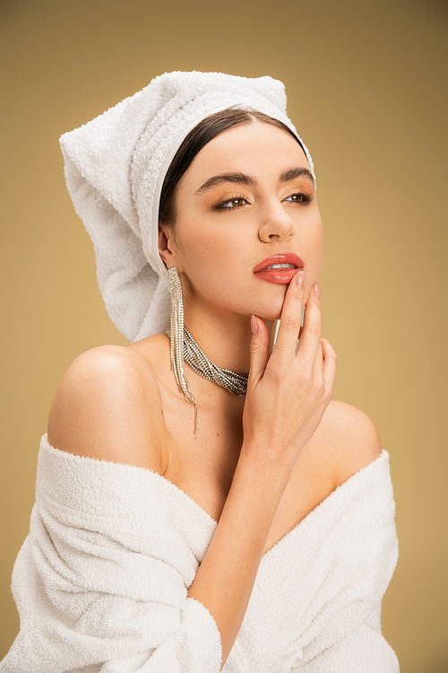 dreamy woman with makeup and towel on head looking away on beige background