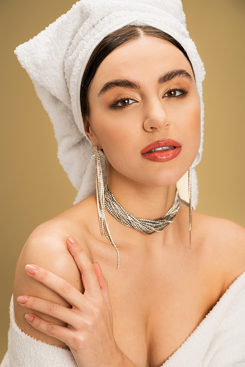 elegant young woman with makeup and towel on head looking at camera on beige background