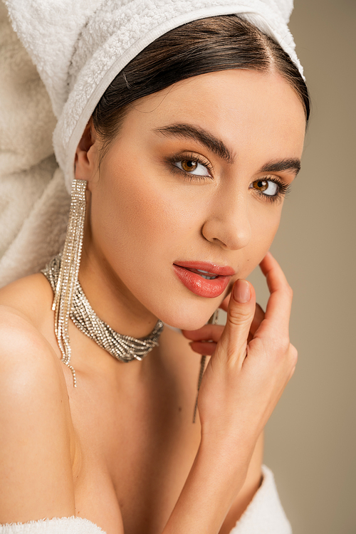 elegant young woman with makeup and jewelry looking at camera on grey