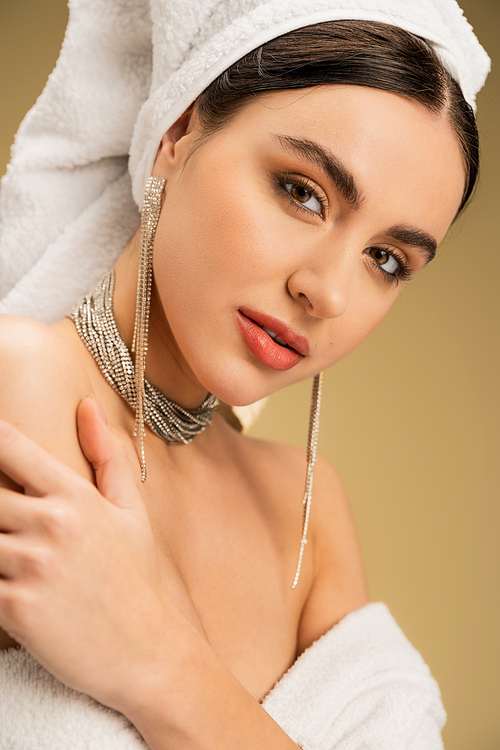 sensual woman with makeup and towel on head looking at camera on beige background