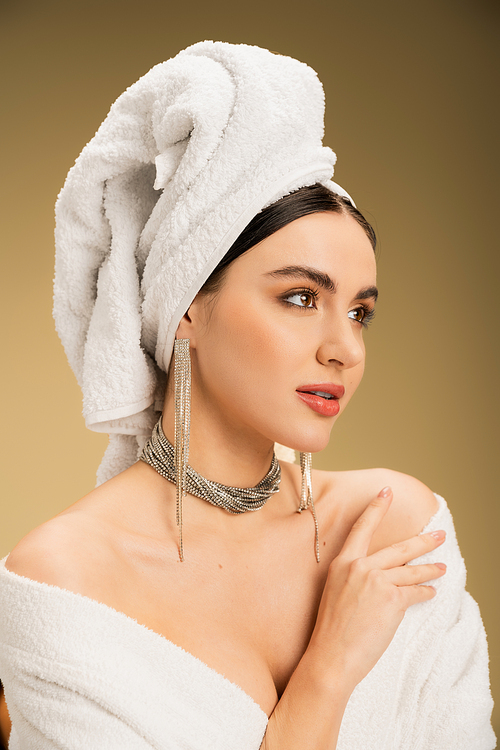 young woman in jewelry with white towel on head looking away on beige background