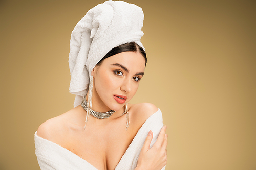charming woman in jewelry with white towel on head looking at camera on beige background