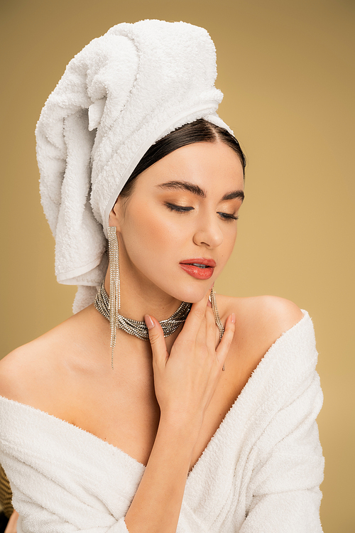 charming woman in jewelry with white towel on head touching chin on beige background