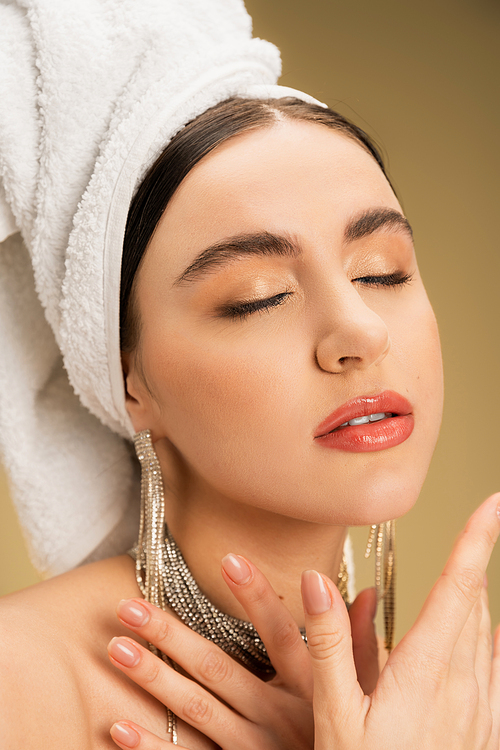 close up view of charming woman in jewelry with white towel on head posing on beige background