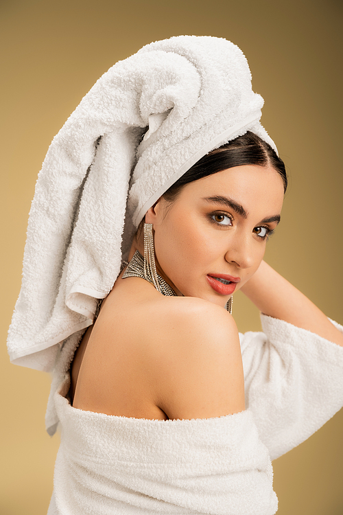 brunette woman with makeup and towel on head looking at camera on beige background