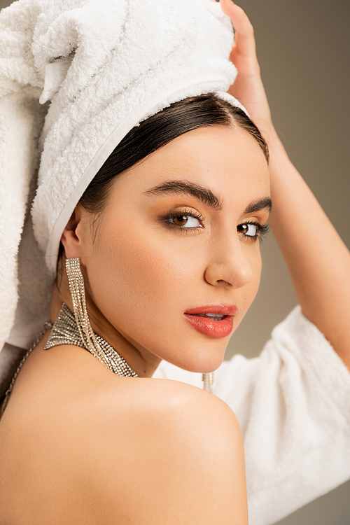 brunette woman with makeup touching white towel on head on grey background