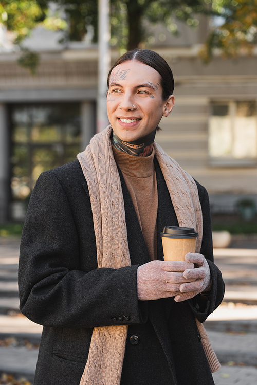 stylish man in coat and scarf smiling while holding paper cup with coffee to go