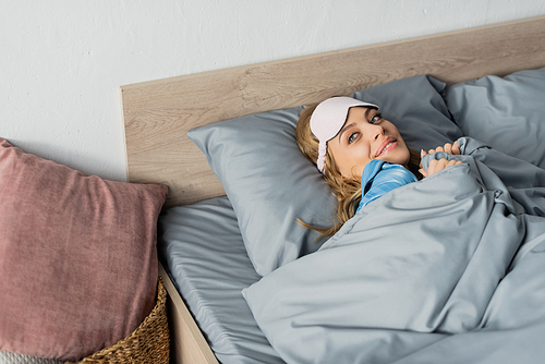 cheerful woman in sleeping mask lying under duvet in comfortable bed