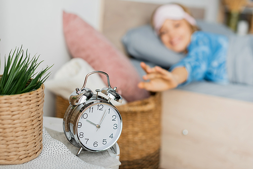 retro alarm clock on bedside table near happy woman in bed on blurred background