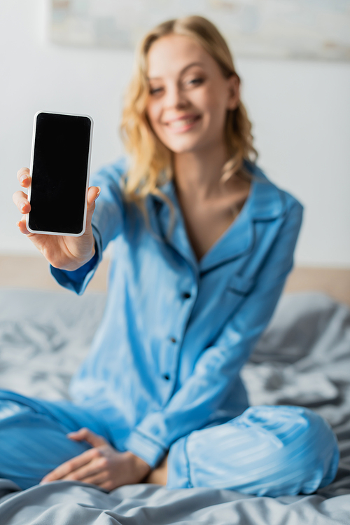 cheerful woman in blue pajama holding smartphone with blank screen