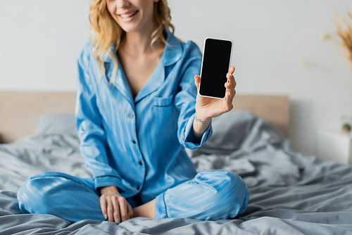 cropped view of pleased woman in blue pajama holding smartphone with blank screen