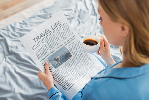 overhead view of young woman reading travel life newspaper and holding cup of coffee in bed