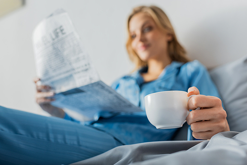 cup of coffee in hand of young woman with newspaper on blurred background