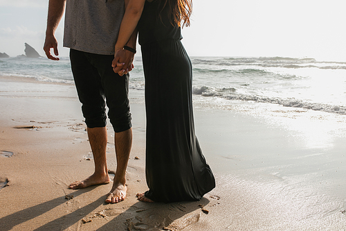 cropped view of man holding hands with girlfriend in dress while standing near ocean