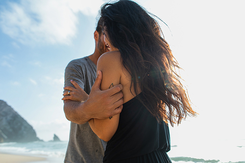 bearded man hugging brunette girlfriend near ocean during vacation