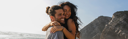 cheerful man hugging tattooed woman on beach, banner