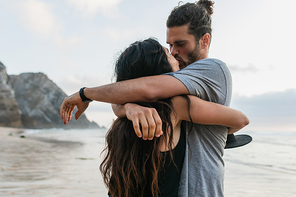 bearded man and brunette woman hugging and kissing on beach in portugal