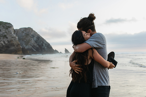 man and brunette woman holding hat and hugging on beach in portugal