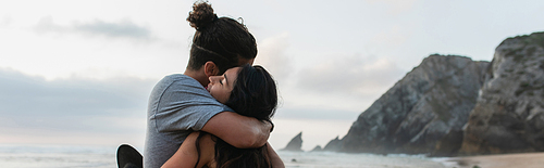 man and brunette woman with closed eyes hugging on beach in portugal, banner