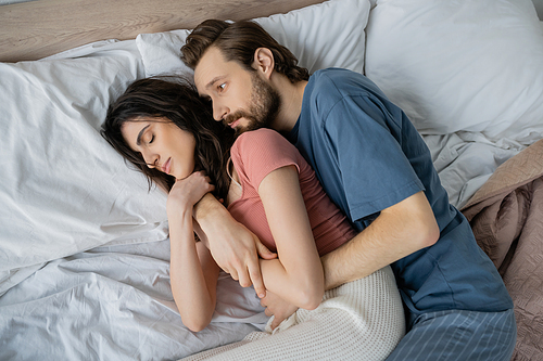 Top view of man in pajama hugging sleeping girlfriend on bed at home