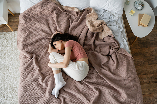 Top view of depressed woman in pajama lying on bed at home