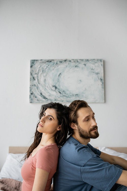 Upset couple in pajama sitting back to back on bed at home