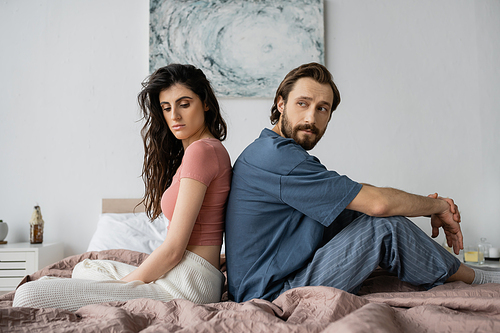 Upset woman in pajama sitting back to back with asexual boyfriend on bed