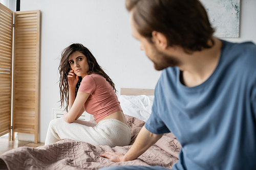 Brunette woman in pajama looking at blurred boyfriend on bed at home