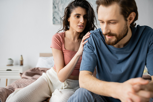 Brunette woman in pajama calming down upset blurred boyfriend on bed