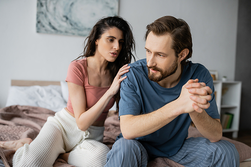 Brunette woman calming down boyfriend with clenched hands in bedroom