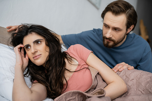 Blurred man looking at brunette girlfriend lying on bed at home