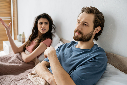 Indifferent man looking away while angry girlfriend quarrelling in bedroom