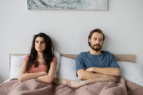 Couple with relationship difficulties crossing arms while sitting on bed at home