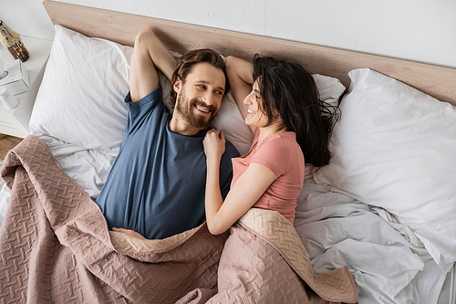 Top view of overjoyed man looking at brunette girlfriend while lying on bed at home