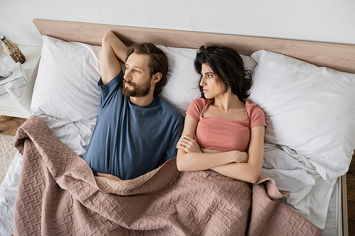 Top view of displeased woman crossing arms and looking at boyfriend on bed at home